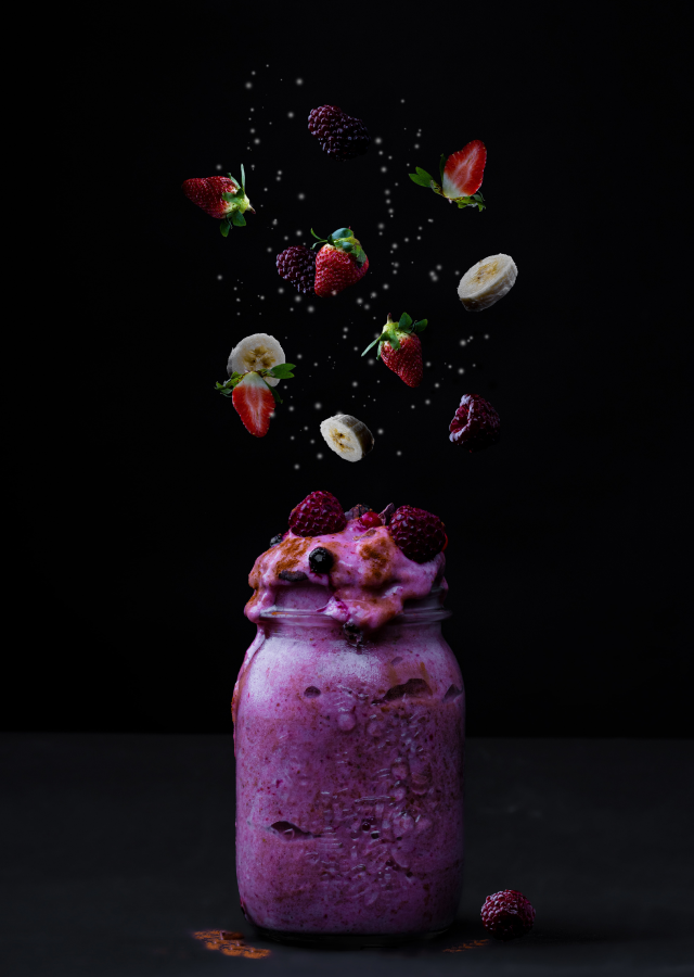 Pote de vidro com sorvete roxo transbordando e frutas flutuando acima dele.
